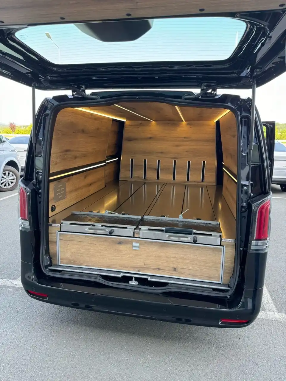 Prazan unutrašnji prostor pogrebnog vozila sa drvenim oblogama, osvetljenjem i metalnim platformama.